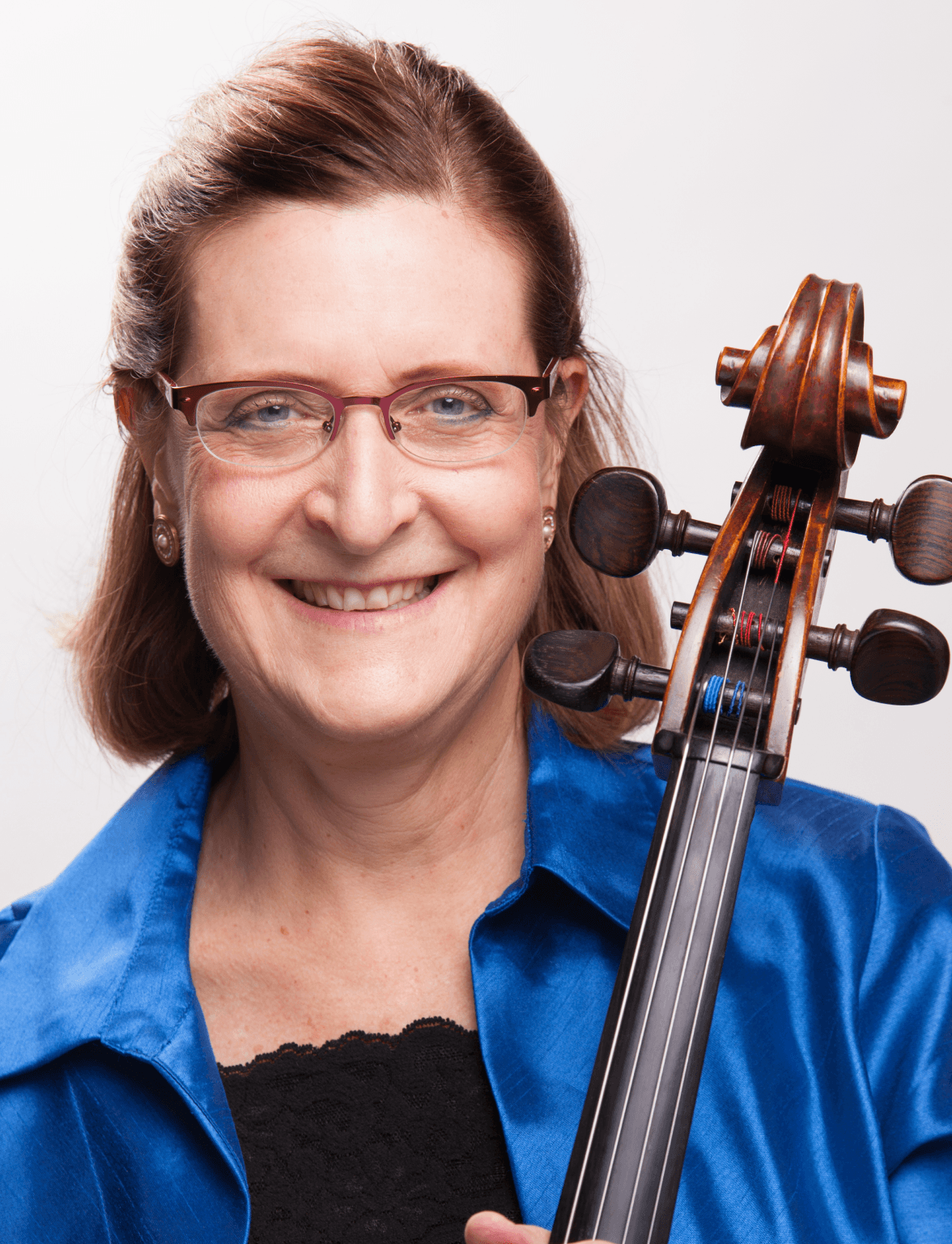 Headshot of Dr. Beth in black lace and blue silk wearing red-framed glasses and smiling at the camera. Her cello is over her left shoulder in playing position.